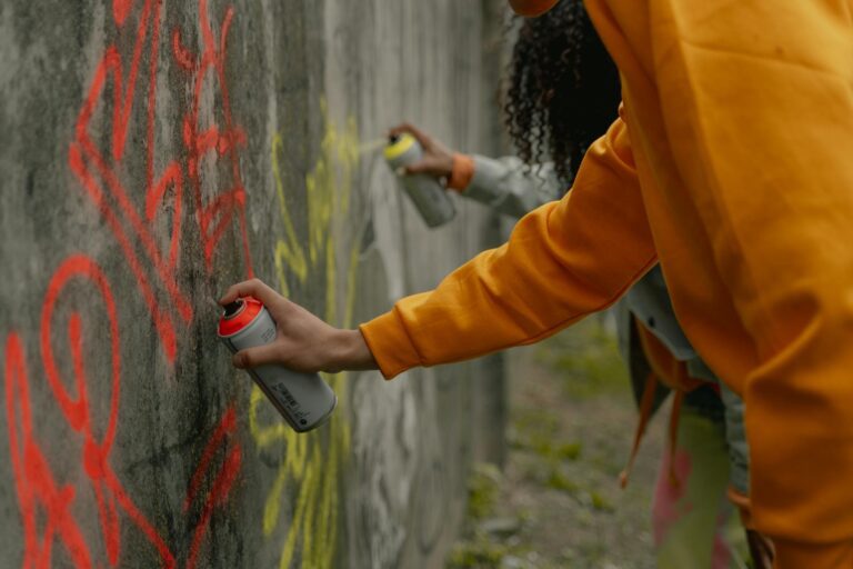 a person in yellow long sleeve shirt spray painting a wall