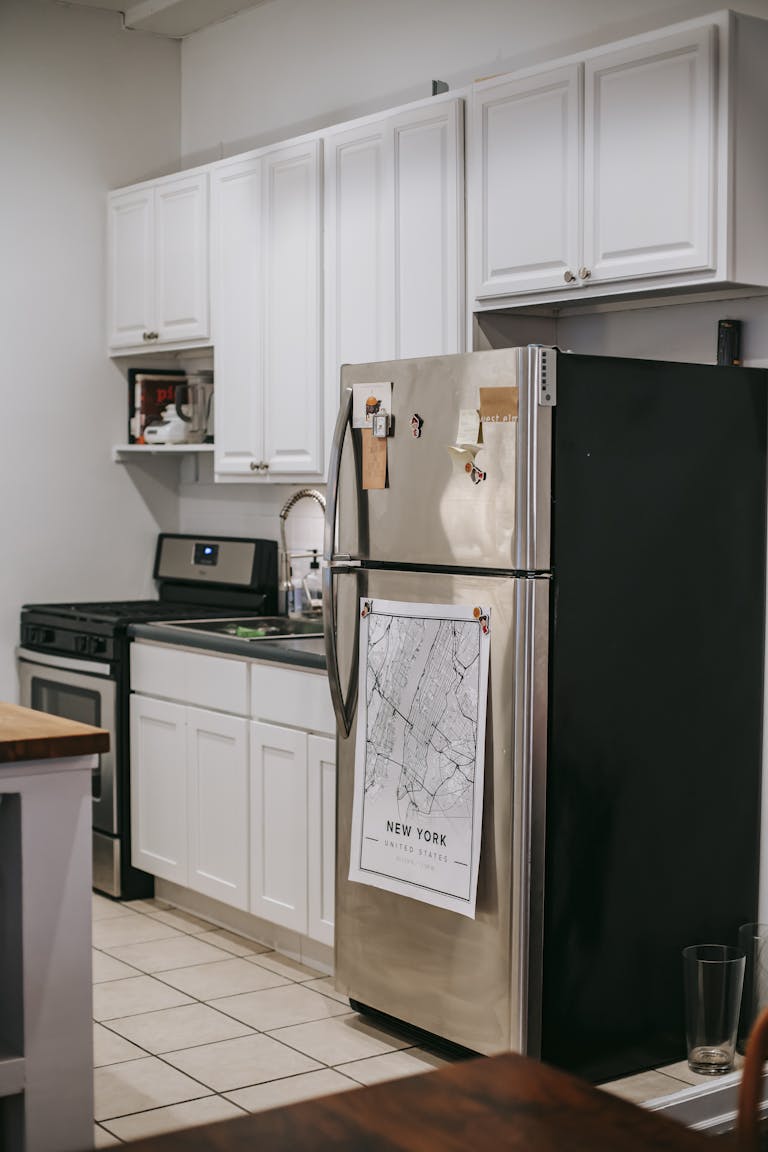 Modern light kitchen furnished with refrigerator and white cupboards placed near stove oven in modern cozy apartment with tiled floor