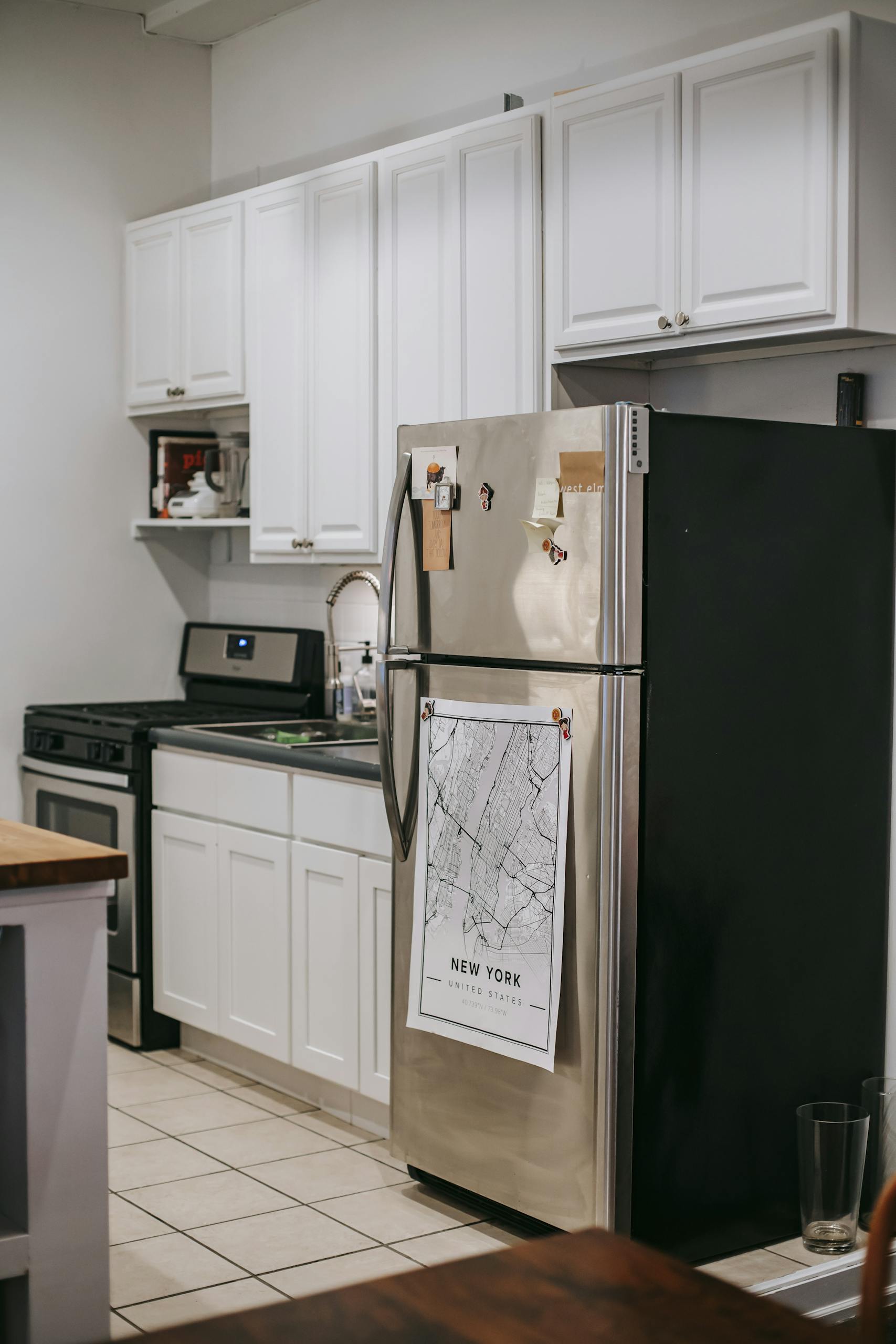 Modern light kitchen furnished with refrigerator and white cupboards placed near stove oven in modern cozy apartment with tiled floor